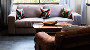 Un salon avec un canapé, une table basse et un banc. Il y a une fenêtre avec des rideaux, et de là, on peut admirer la verdure à l’extérieur.