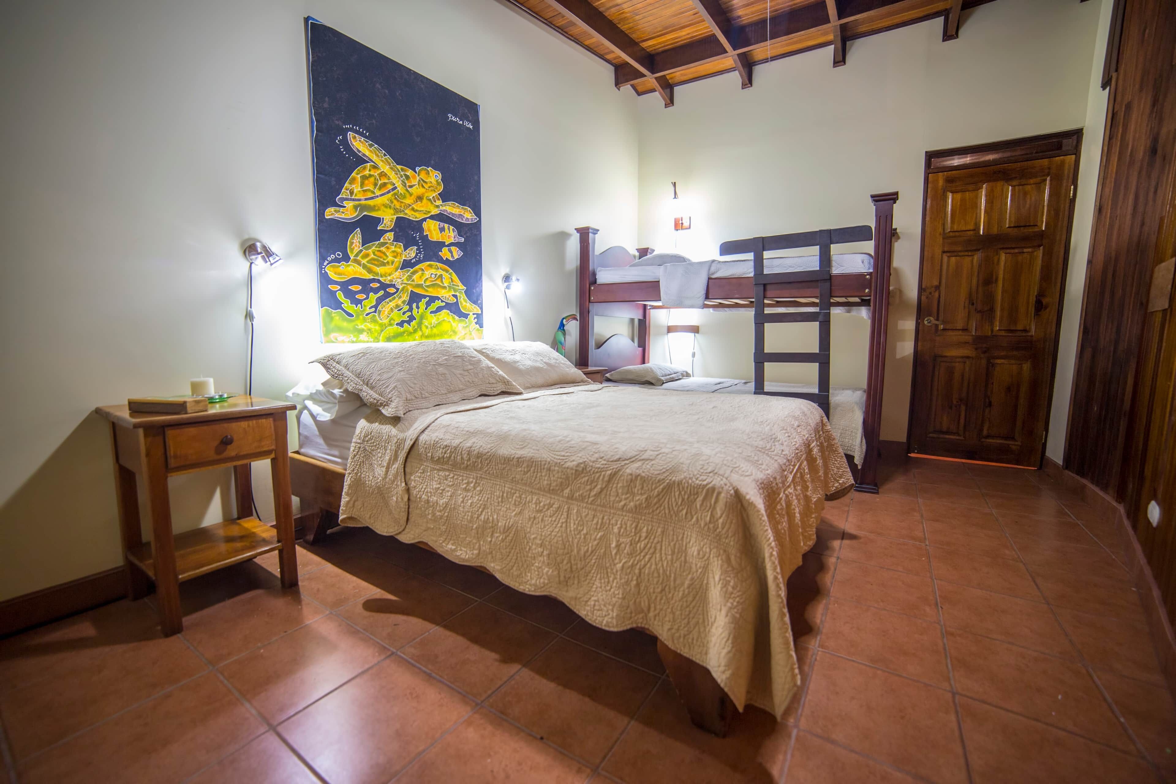 A bedroom with a bed, a nightstand, a wooden ladder, a door, and a wall with a mural.