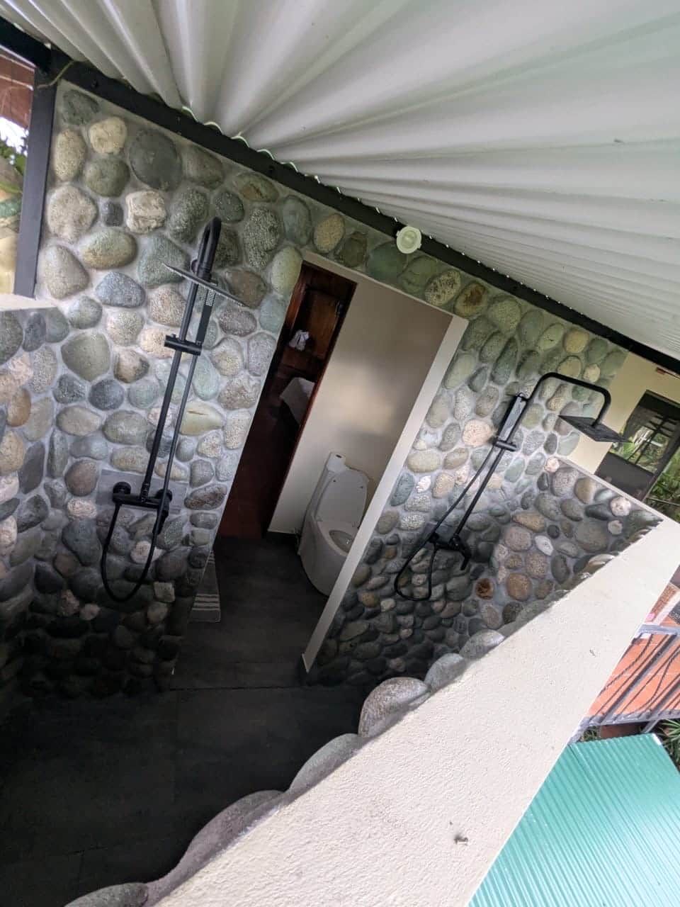 A stone-walled bathroom with two showerheads and a toilet.