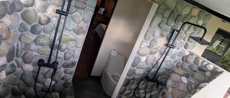 A stone-walled bathroom with two showerheads and a toilet.