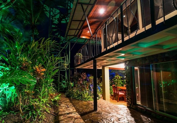 A covered outdoor area with a stone pathway leading to a seating area, surrounded by lush tropical plants.