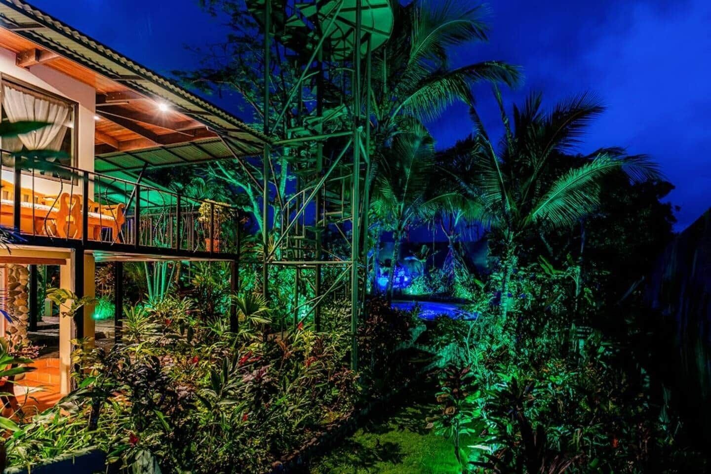A modern house with a glass balcony overlooking a lush garden at night.
