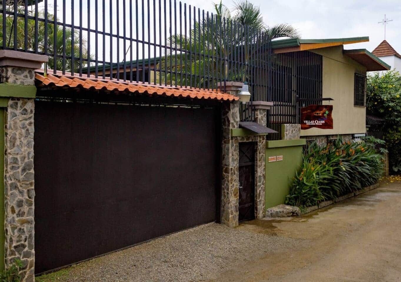 A gated property with a closed garage door, stone pillars, and a sign indicating 'Villas Oasis'.