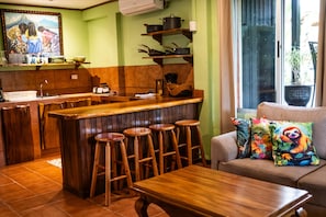 A kitchen with wooden stools, a bar counter, and a sofa with colorful cushions.