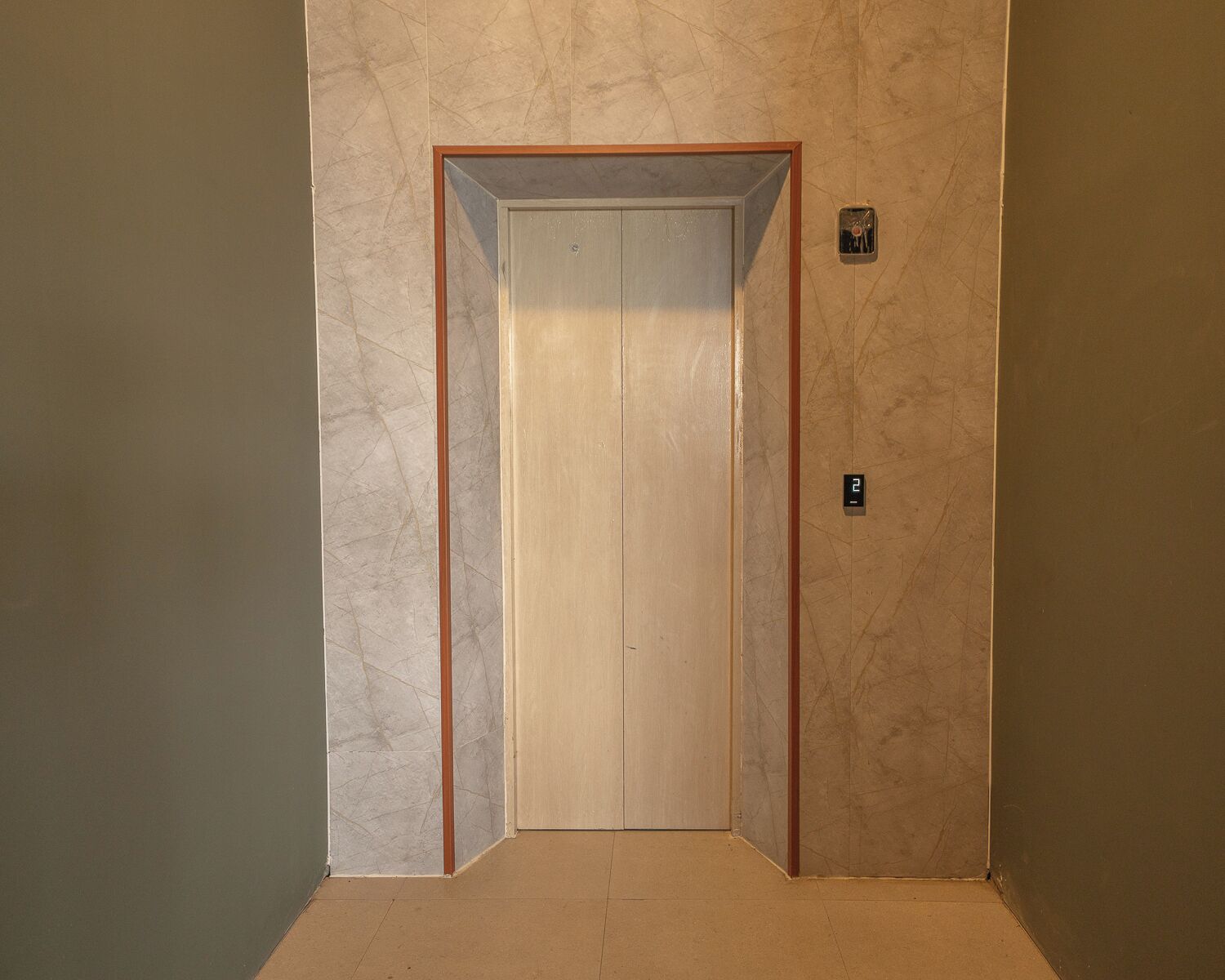 A closed elevator door with a marble wall and a small digital display above it.