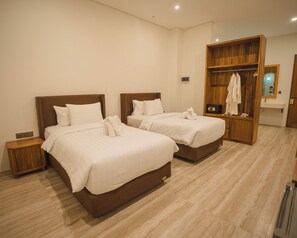 A hotel room with two beds, a wooden wardrobe, a bedside table, and a bathroom with a mirror and towel rack. - Tribhuwana Padma Lake Resort (Kintamani)