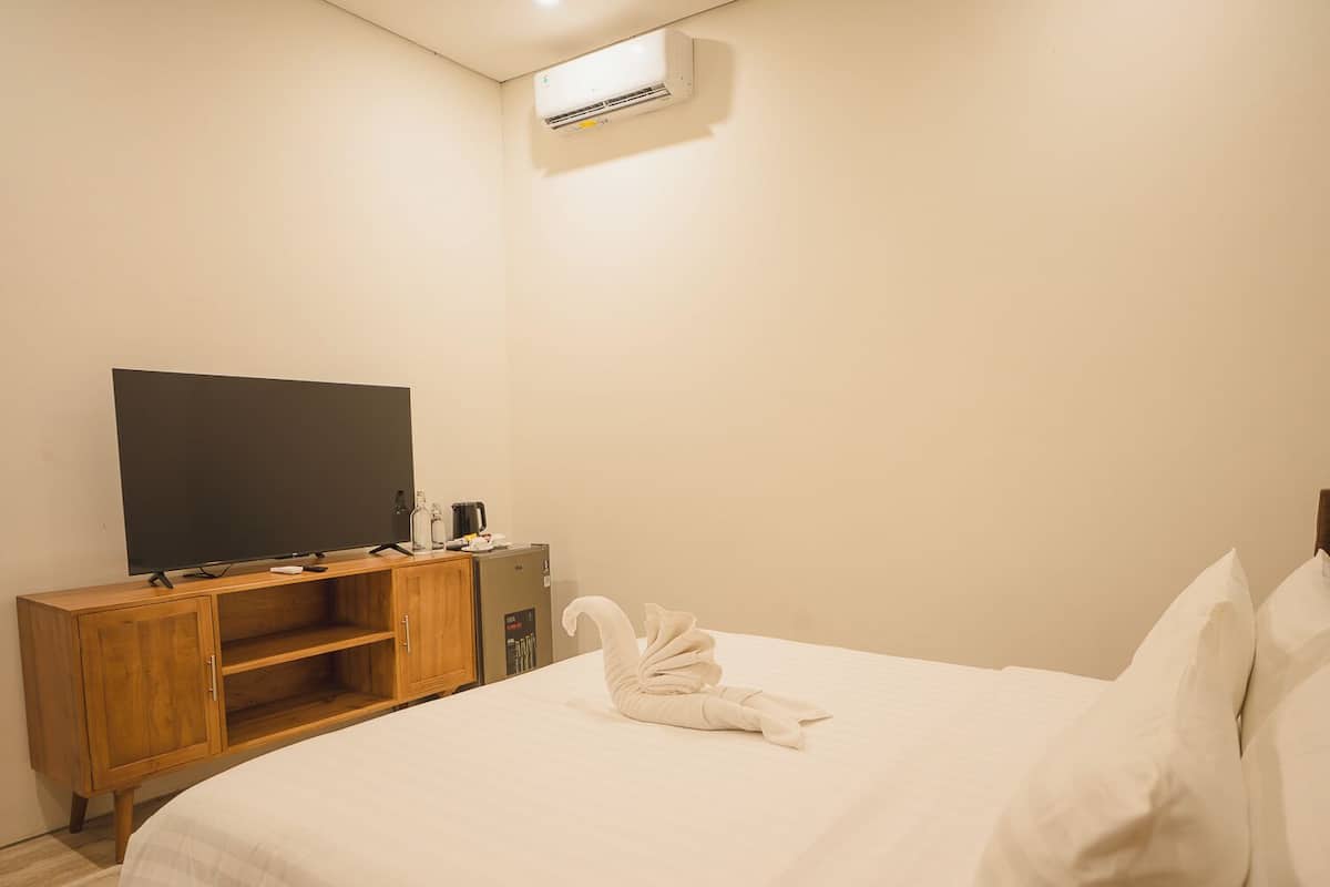 A hotel room with a bed, a TV on a wooden stand, a minibar, and a wall-mounted air conditioner.