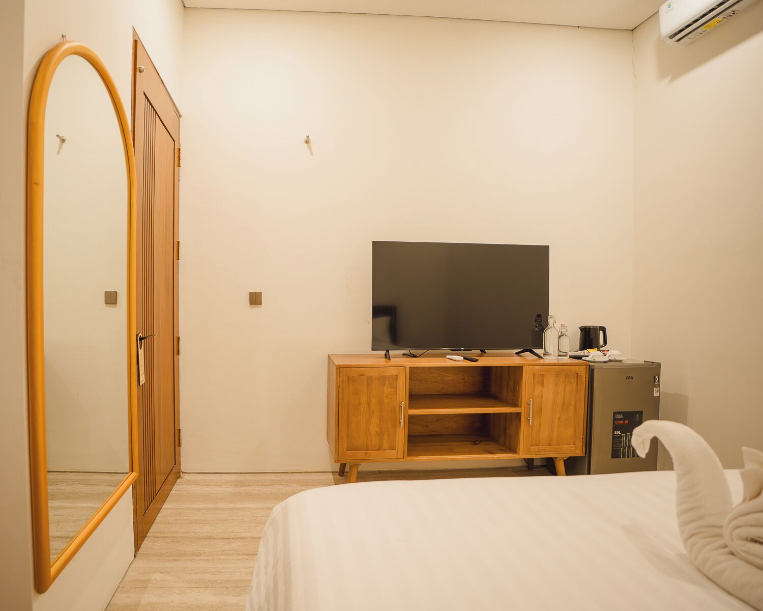 Egy szállodai szoba, amelyben található egy ágy, egy fából készült szekrény, egy síkképernyős televízió, egy minibar és egy nagy tükör.
