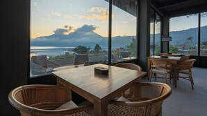 A dining area with a view of the sea and mountains, featuring wooden tables and wicker chairs. - Tribhuwana Padma Lake Resort (Kintamani)