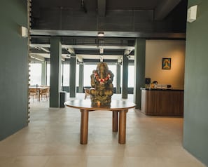 Uma área de recepção com uma mesa de madeira redonda, uma estátua e um balcão de atendimento.