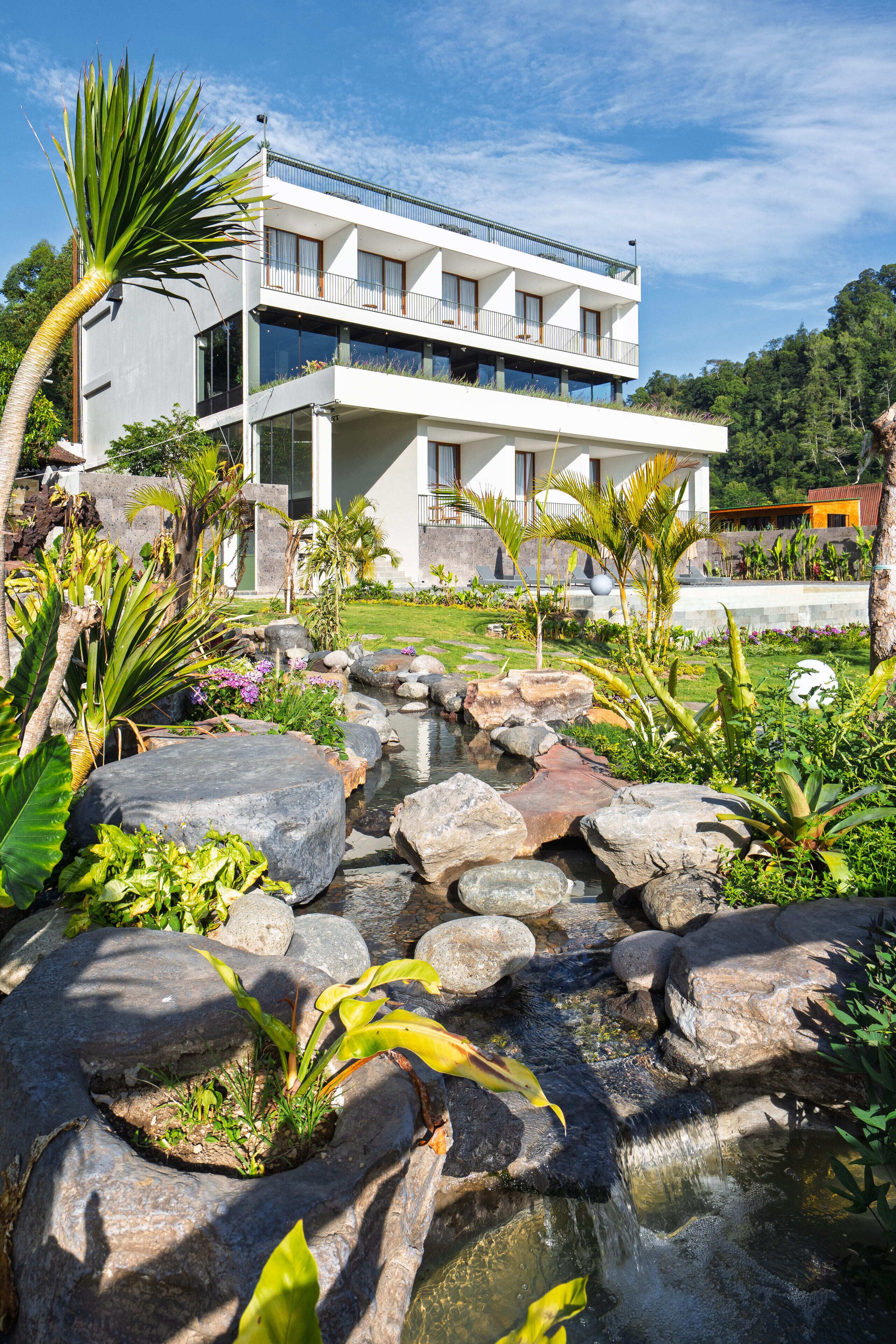 A modern two-story building with a landscaped garden featuring a small waterfall and large rocks.