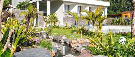 A modern two-story building with a landscaped garden featuring a small waterfall and large rocks.
