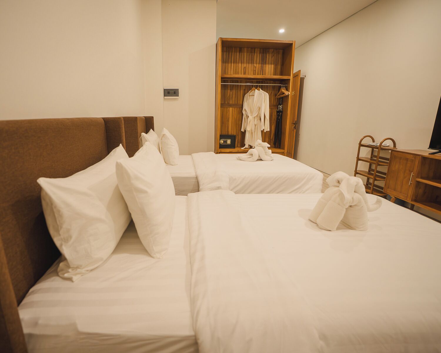 A hotel room with two beds, a wooden wardrobe, and a television.