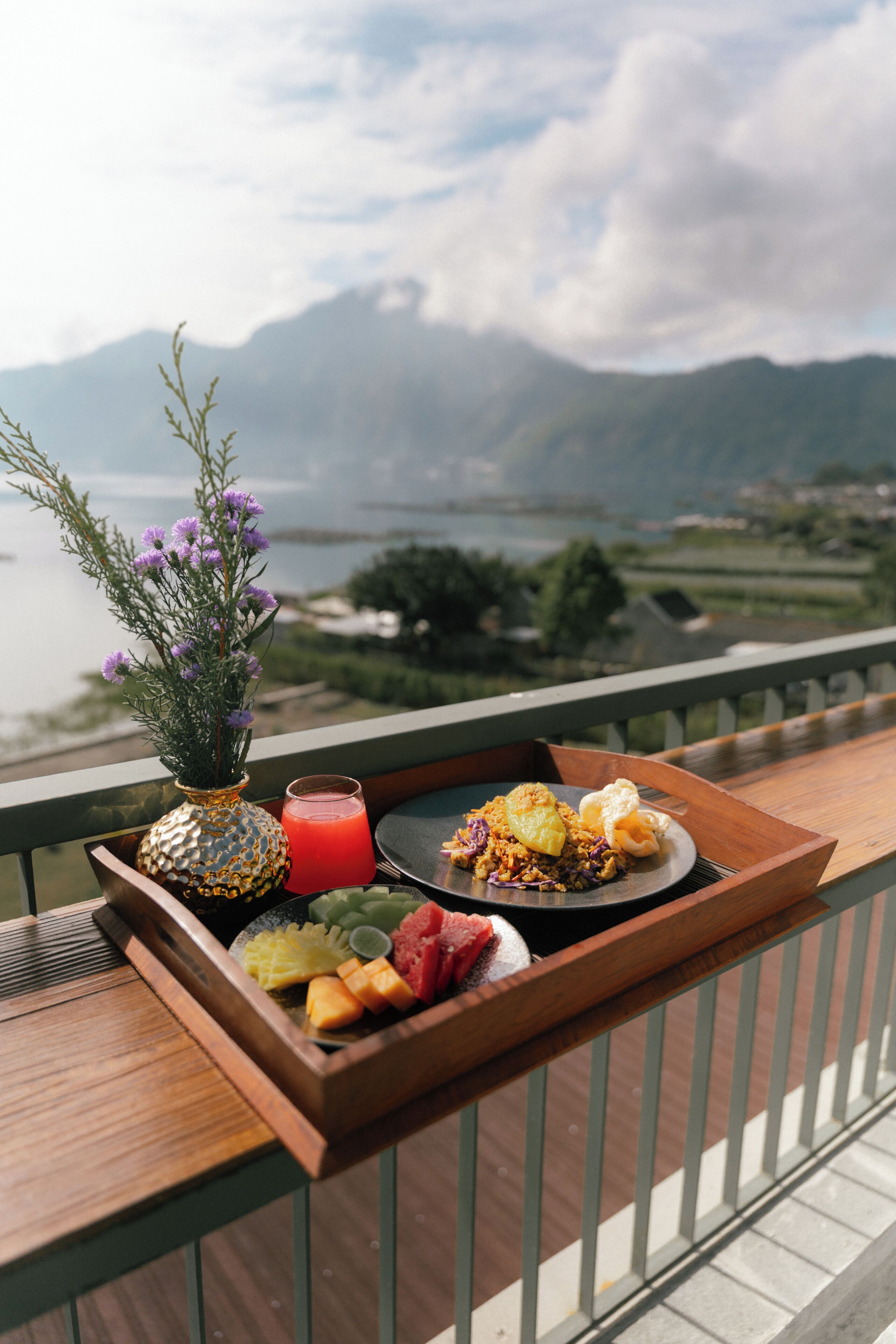 A tray with food and a drink on a balcony overlooking a mountainous landscape.