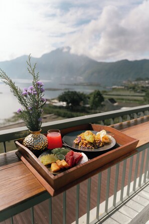 Un plateau avec de la nourriture et une boisson, posé sur un balcon donnant sur un paysage montagneux.