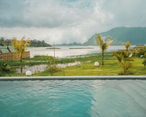 A swimming pool with a view of a calm lake, surrounded by greenery and palm trees. - Tribhuwana Padma Lake Resort (Kintamani)