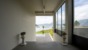 A modern hallway with a view of a lake and mountains. There are two potted plants on pedestals. - Tribhuwana Padma Lake Resort (Kintamani)