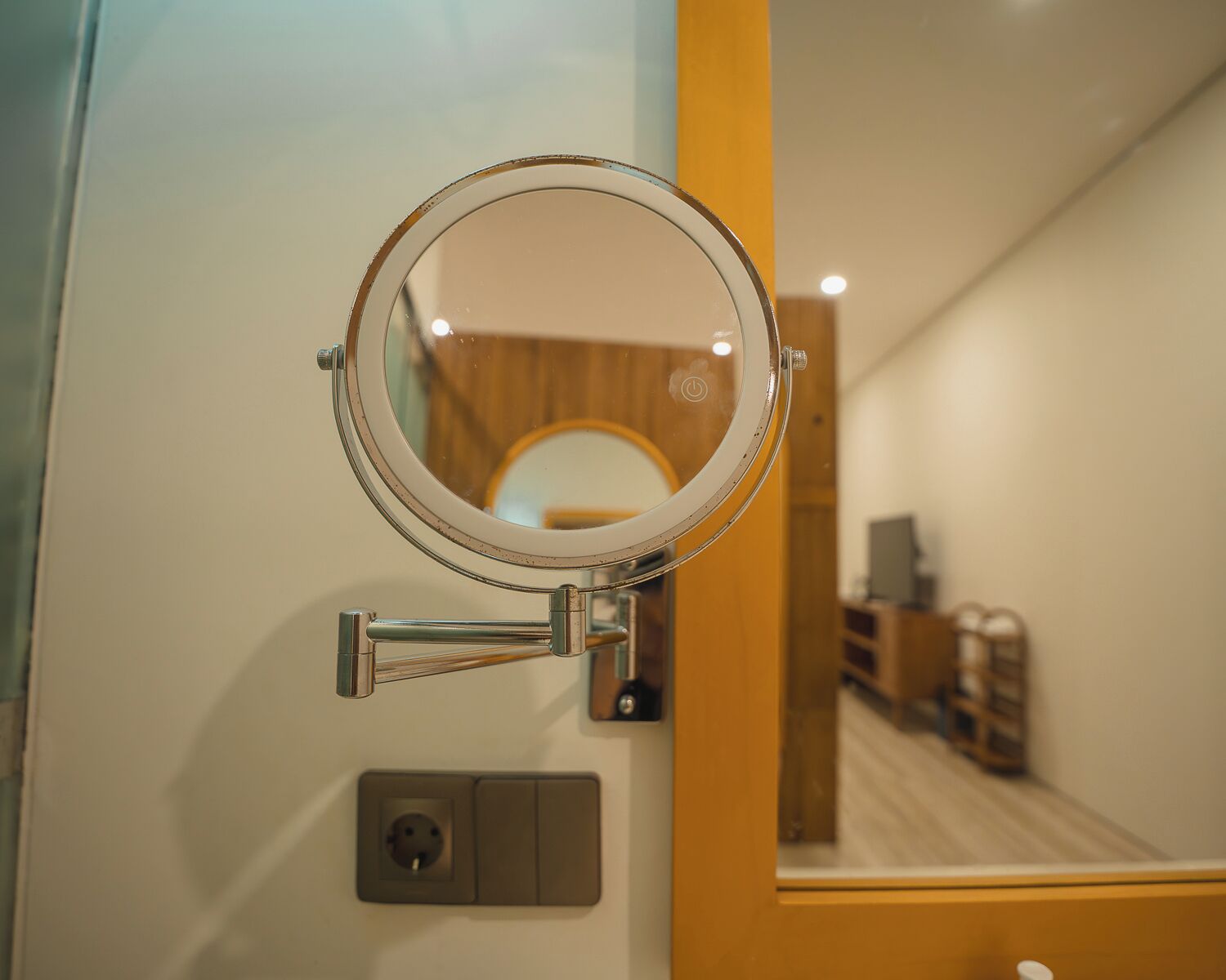 A bathroom with a round mirror mounted on the wall, a light switch, and a reflection of a wooden interior.