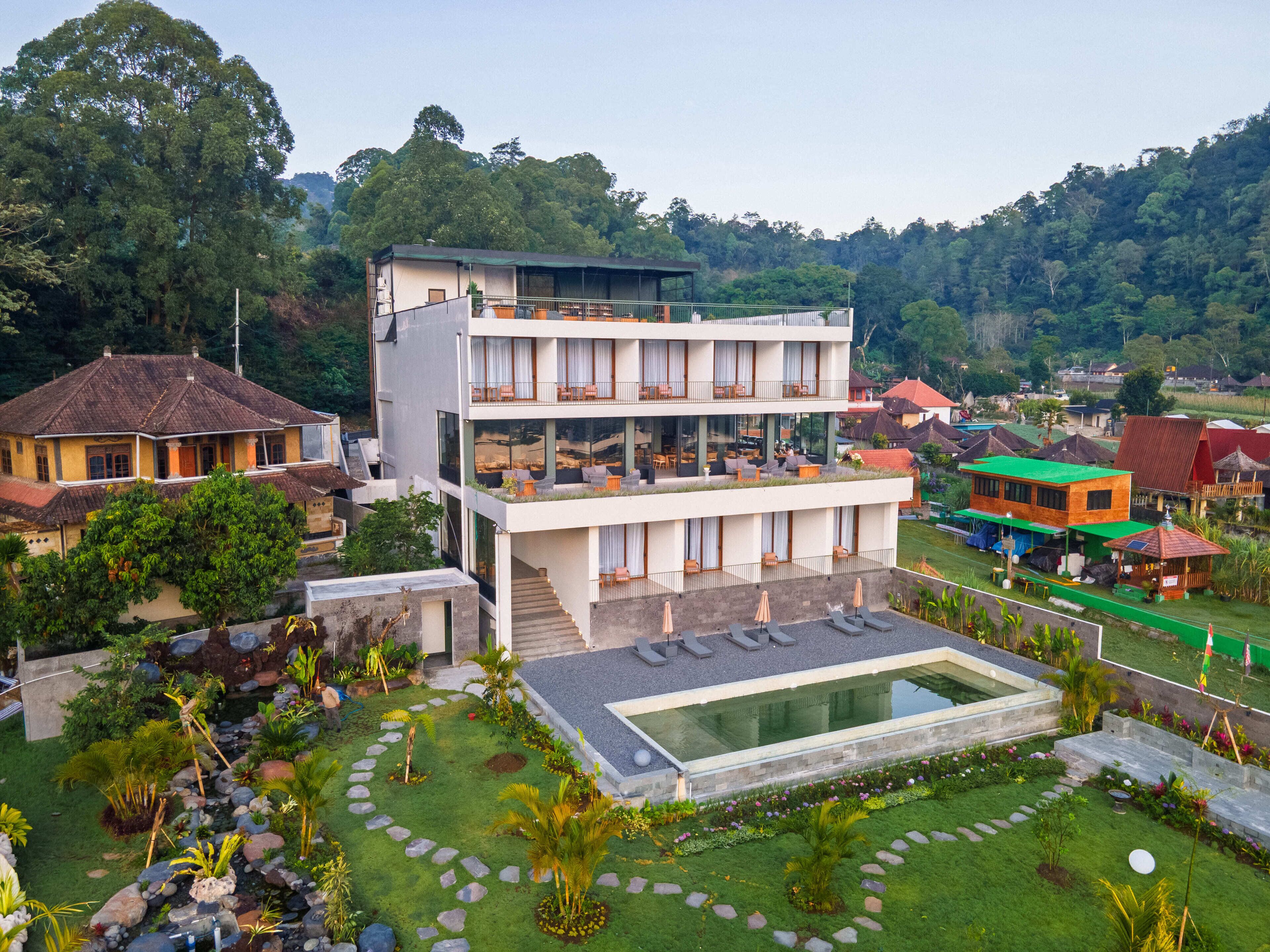 A modern multi-story hotel with a rooftop pool and a lush garden.
