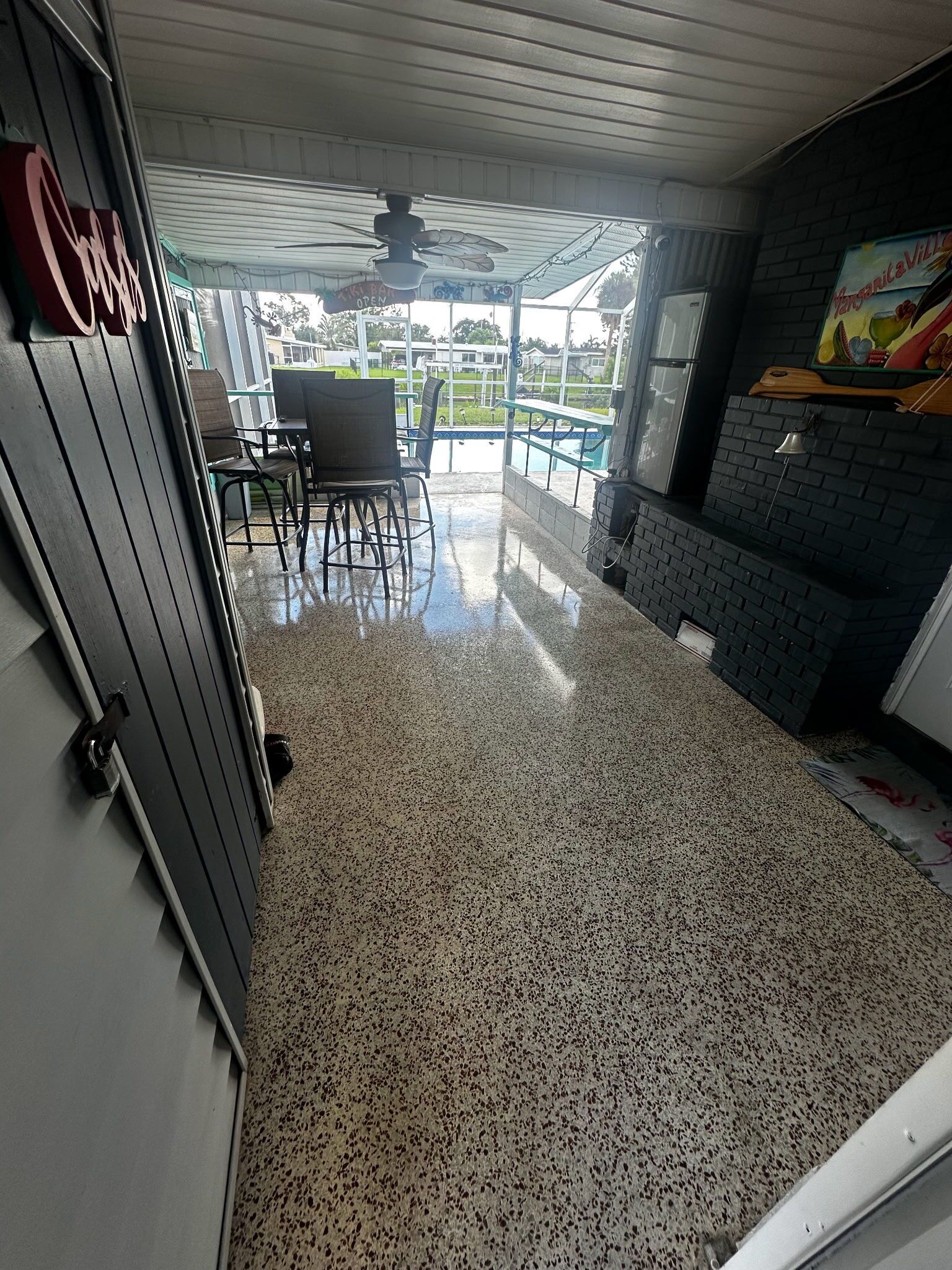 A spacious indoor area with a terrazzo floor, a ceiling fan, and a view of a swimming pool.