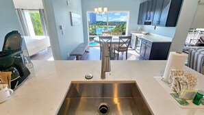 Eine moderne Küche mit Spüle aus Edelstahl, ein Essbereich mit Blick auf einen Pool und ein Balkon mit Blick auf eine Stadtlandschaft.