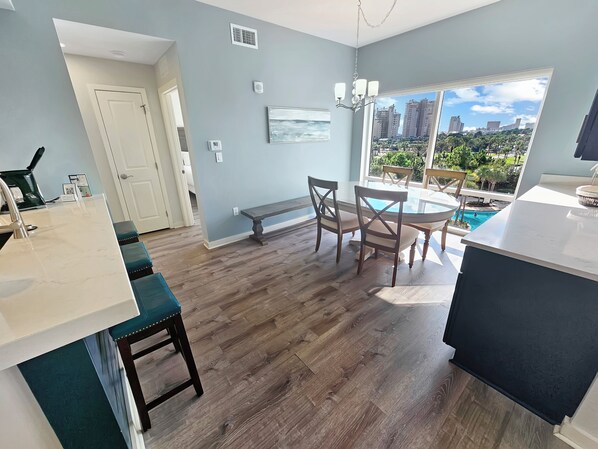A modern kitchen with a dining area, a large window with a city view, and a pool visible through the window. - Luau 6424 | 1BR Condo w/ Gulf Views, Pool Views & Steps to the Beach (Miramar Beach)