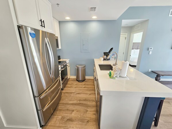 A modern kitchen with stainless steel appliances, a white countertop, and a wooden floor. - Luau 6424 | 1BR Condo w/ Gulf Views, Pool Views & Steps to the Beach (Miramar Beach)