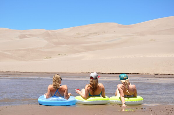Three people sitting on inflatable tubes on a sandy beach with dunes in the background. - Mountain Oasis Great for Families and Groups Sleeps 8+ (Poncha Springs)