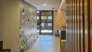 A hallway with a mural of a cityscape, a glass door leading outside, and a modern interior design with a wooden slat wall and hanging pendant lights.