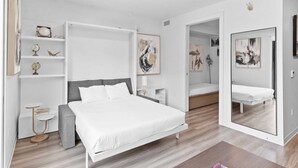 A modern bedroom with a white bed, a bedside table, a small round table, and a mirror.