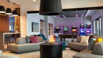 A modern living room with a fireplace, sofas, a pool table, and arcade games.