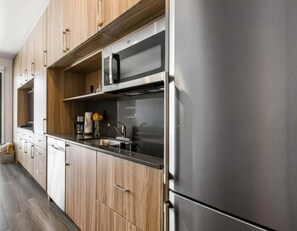 A modern kitchen with wooden cabinets, a stainless steel refrigerator, and a microwave.