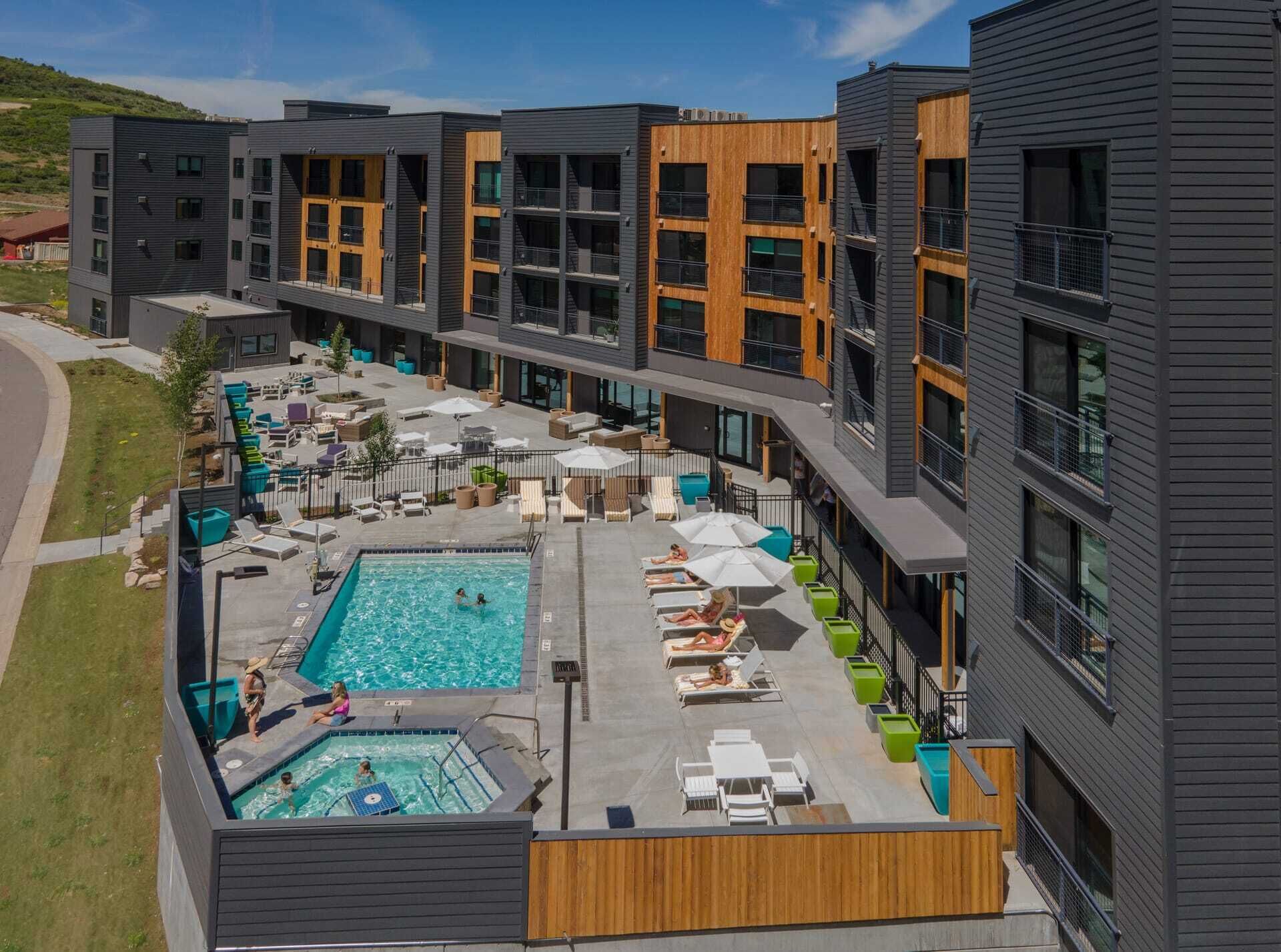 A modern building with a rooftop pool area, outdoor seating, and a clear view of the surrounding landscape.