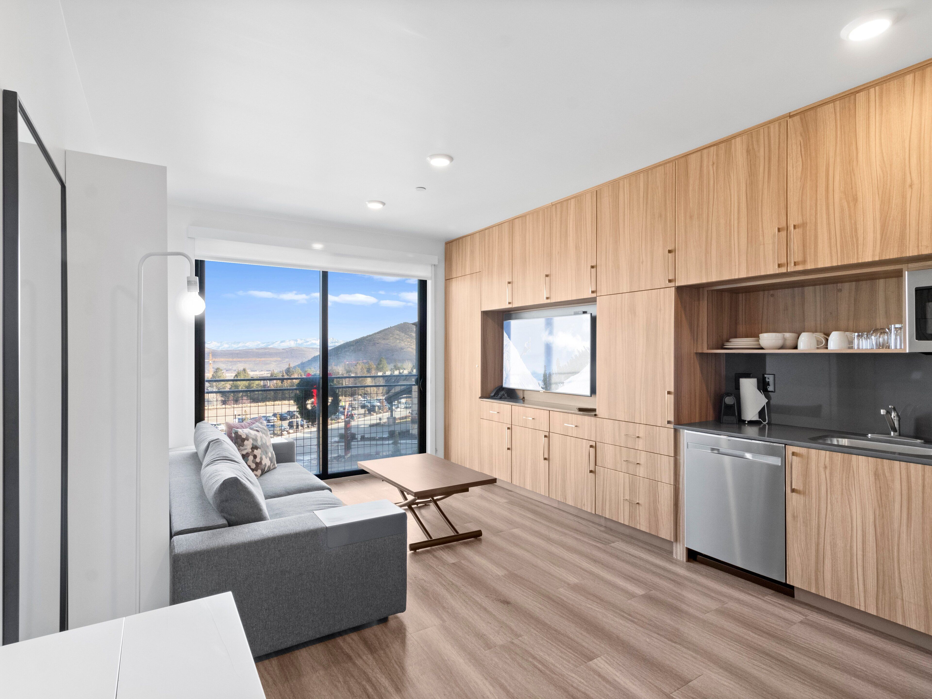 Una cocina moderna con armarios de madera, horno empotrado y un amplio ventanal con vistas a un paisaje montañoso.