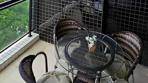 A balcony with a glass table and wicker chairs, a view of a cityscape, and a black mesh partition. - Luxury Celebration Apartment - Belém, PA (Belém)
