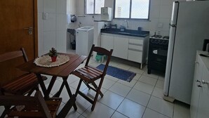 A compact kitchen with white cabinets, a dining table with chairs, a refrigerator, and a window providing natural light. - Luxury Celebration Apartment - Belém, PA (Belém)