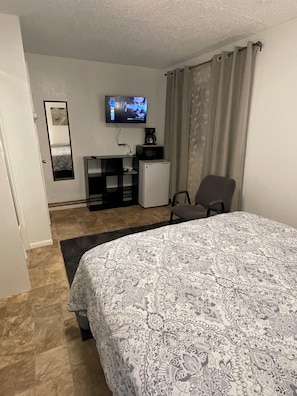 Una habitación de hotel con cama, escritorio con computadora, televisor y cafetera.