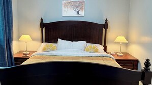 A neatly made bed with a dark wooden headboard, two bedside lamps, a painting on the wall, and a blue curtain. - Terrific 3-bedroom apartment in Fairbanks (Fairbanks)