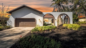 A modern house with a garage, arched entryway, and landscaped garden.