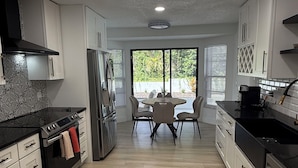A modern kitchen with white cabinets, a black countertop, and a dining area with a table and chairs.