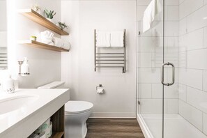 A modern bathroom with a toilet, a shower with a glass door, and a sink with a wooden shelf above it.