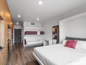 Quarto de hotel moderno com beliche, escrivaninha e uma cama grande.