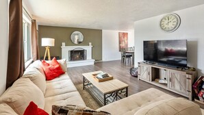 Una sala de estar con sofá, mesa de centro, televisor, chimenea y un reloj en la pared.