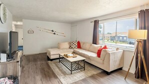 Una sala de estar con un sofá modular, un televisor, una mesita de centro y una ventana con cortinas.
