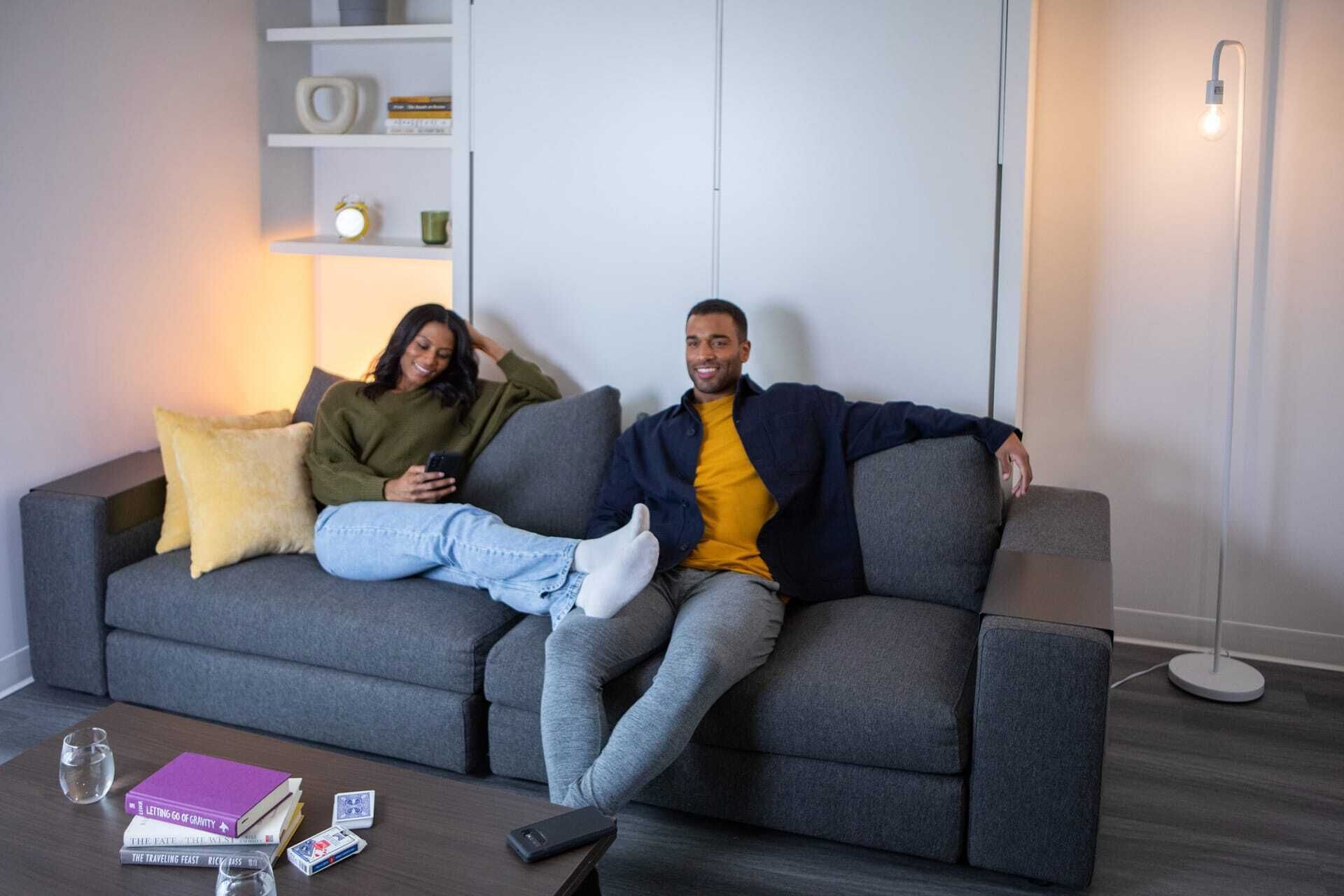 En moderne stue med en grå sofa, et sofabord med bøger og spillekort, og en gulvlampe.