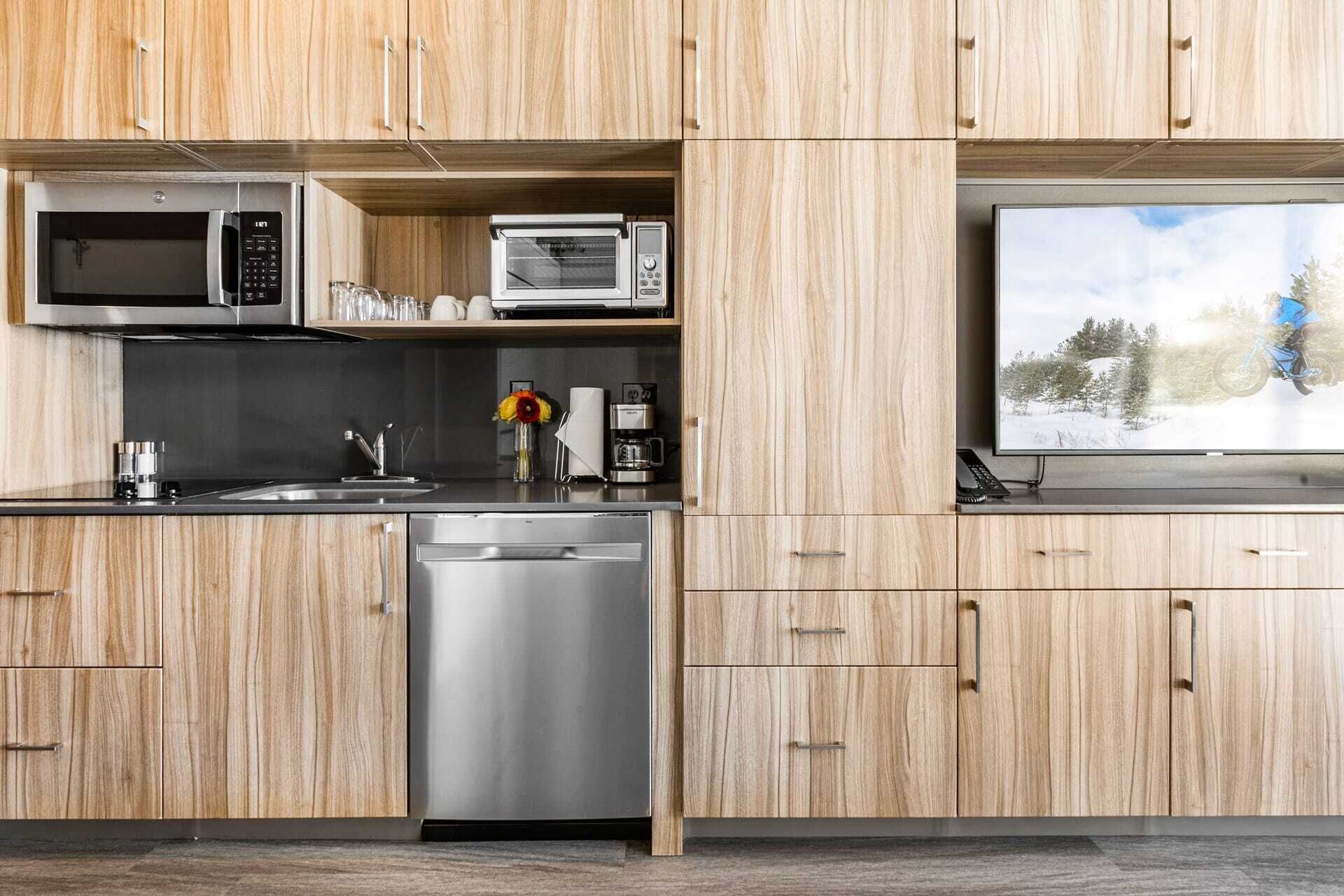 A modern kitchen with wood cabinetry, stainless steel appliances, and a built-in window with a snowy landscape view.