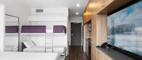 Una habitación de hotel moderna con literas, un armario de madera, un televisor de pantalla plana y una pequeña mesa de madera.