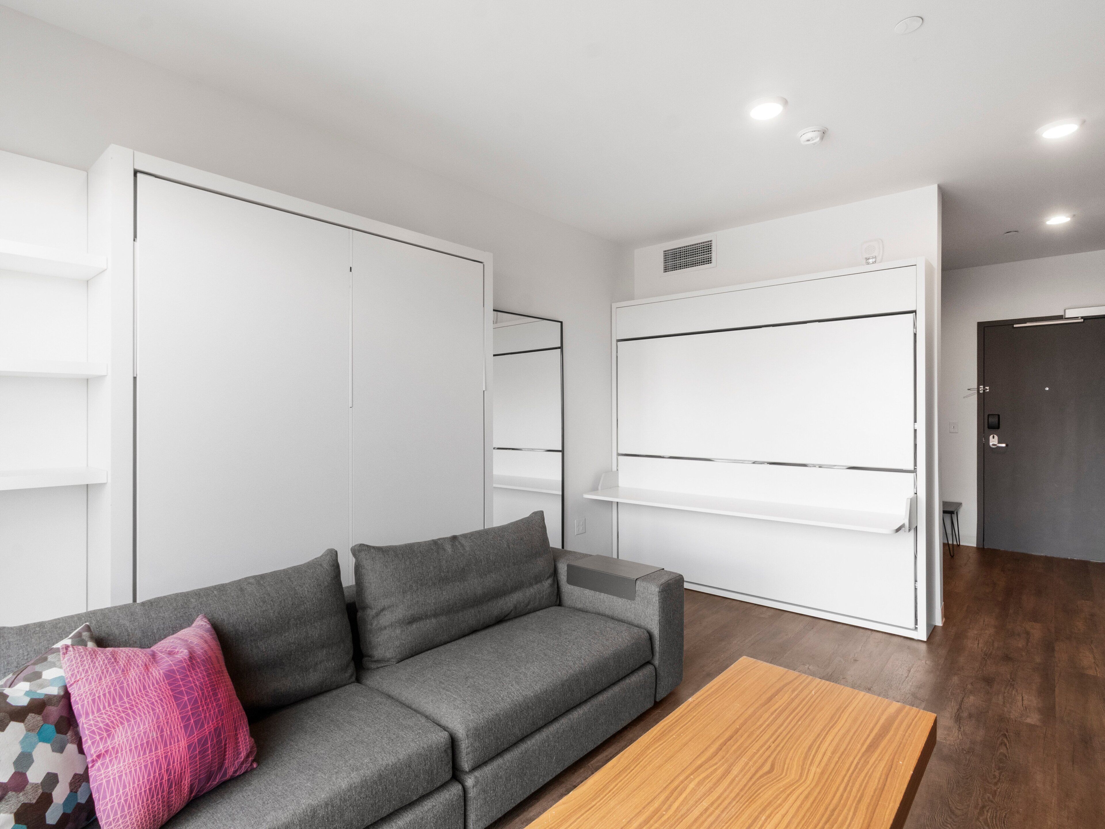 A modern living room with a grey sofa, a wooden coffee table, and a large white wardrobe.