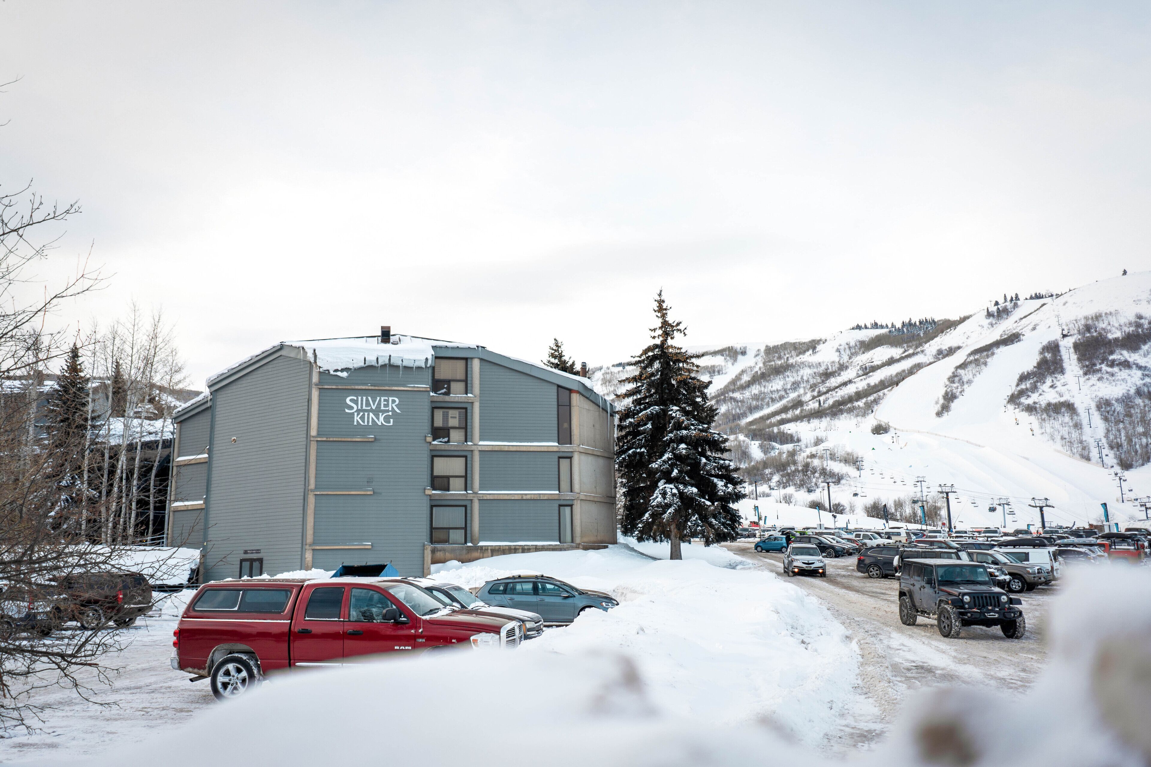 A building with the sign "Silver King" in a snowy parking lot with cars and a mountain in the background.