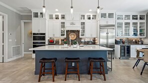 A modern kitchen with white cabinets, a central island with stools, and a sign reading "Welcome to Love Shack".